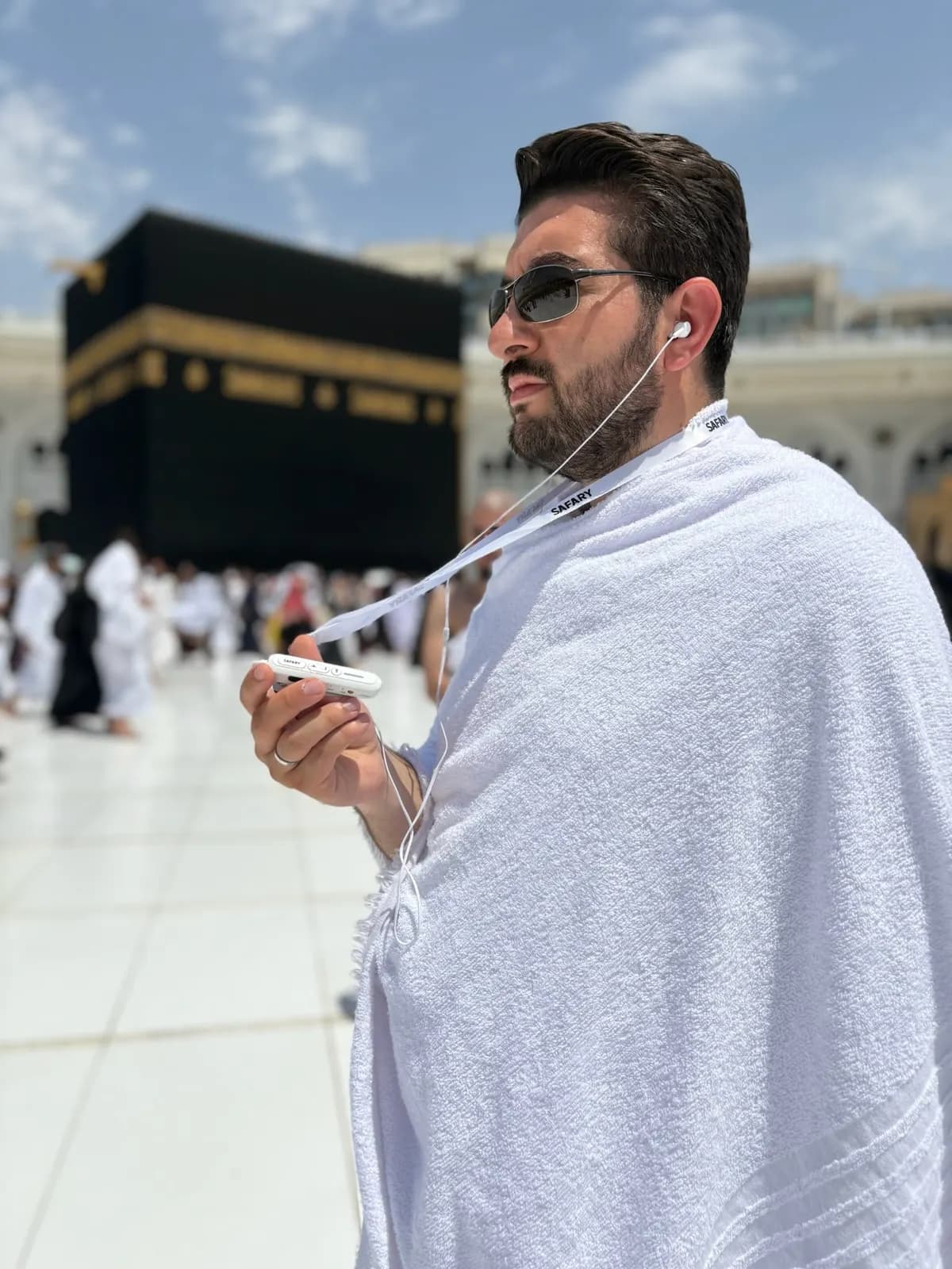 İhramlı bir misafir Kâbe önünde kulaklıkla rehberlik cihazını dinliyor